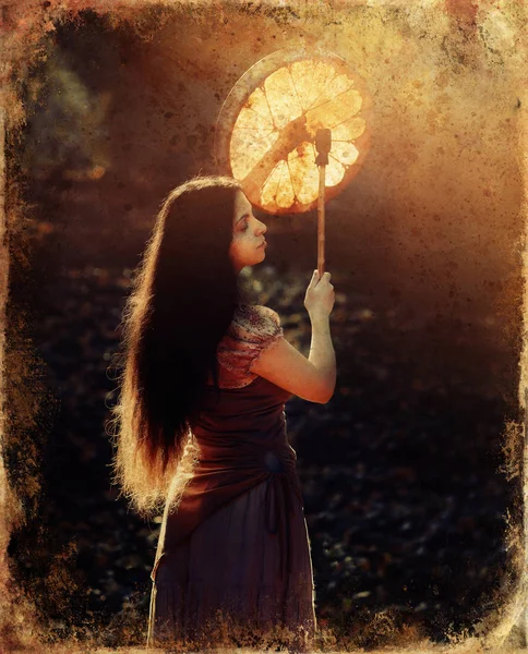 Beautiful shamanic girl playing on shaman frame drum in the nature, old photo effect. — Stockfoto