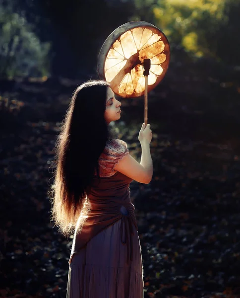 Beautiful shamanic girl playing on shaman frame drum in the nature. — Stock Photo, Image