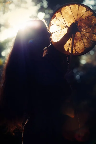 Bella ragazza sciamanica che gioca sul tamburo telaio sciamano nella natura. — Foto Stock