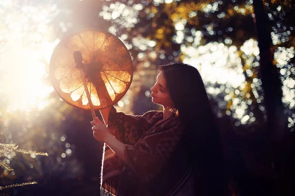 Hermosa chica chamánica jugando en tambor marco chamán en la naturaleza. — Foto de Stock