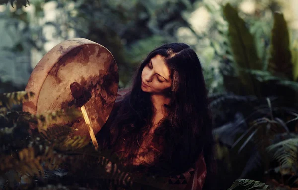 Beautiful shamanic girl playing on shaman frame drum in the sunlight. — Stockfoto