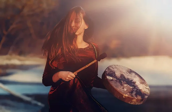 Bela garota xamânica jogando no tambor quadro xamã na natureza e efeito gráfico de luz . — Fotografia de Stock