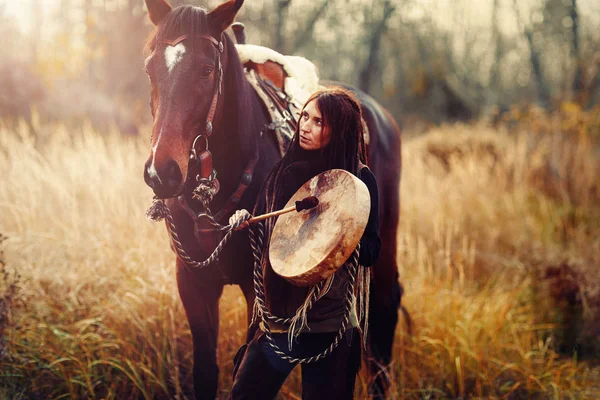 Young dreadded girl with her horse and shamanic frame drum. — Stock Photo, Image