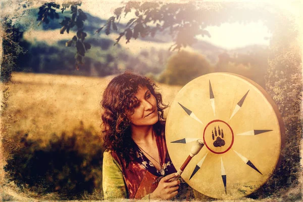 Beautiful shamanic girl playing on shaman frame drum in the nature, old photo effect. — ストック写真