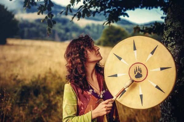 Hermosa chica chamánica jugando en tambor marco chamán en la naturaleza. —  Fotos de Stock