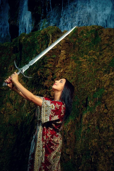 Mulher com espada no lago perto da cachoeira. — Fotografia de Stock