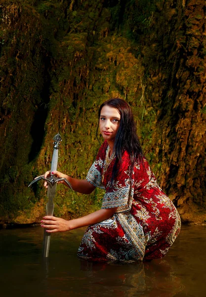 Mulher com espada no lago perto da cachoeira. — Fotografia de Stock