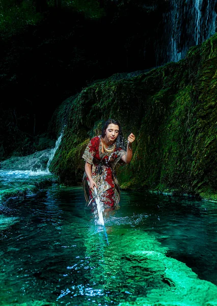 Donna con spada nel lago vicino alla cascata. — Foto Stock