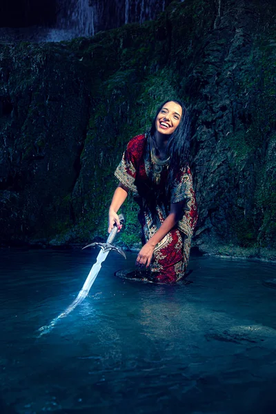 Mulher com espada no lago perto da cachoeira. — Fotografia de Stock