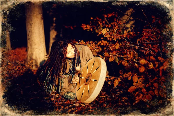 Beautiful shamanic girl playing on shaman frame drum in the nature, old photo effect. — Stockfoto