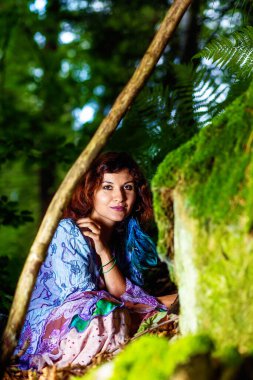 Ormanlık alanda kayaların yanında oturan renkli elbiseli kız.