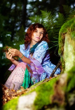 Ormanlık alanda kayaların yanında oturan renkli elbiseli kız.