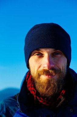 Arkasında mavi gökyüzü ve kış şapkası olan dondurucu genç adam.