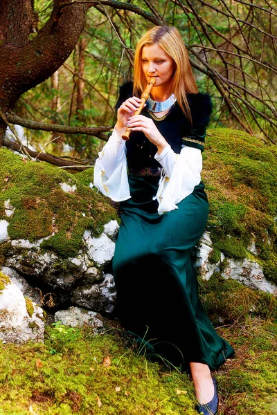 穿着历史服装的漂亮姑娘在森林里吹奏长笛 和浅色的图形效果 — 图库照片