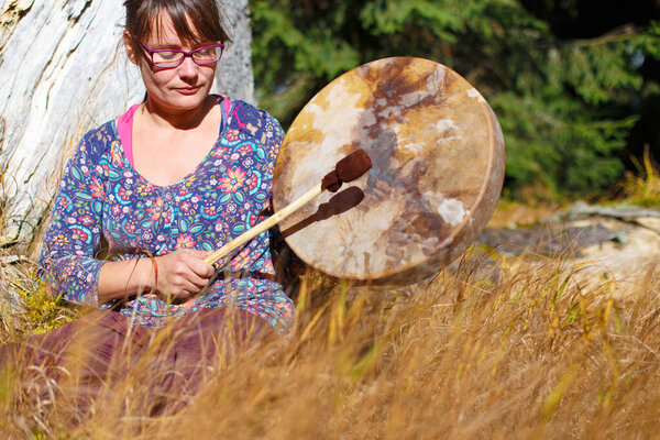 beautiful shamanic girl playing on shaman frame drum in the nature