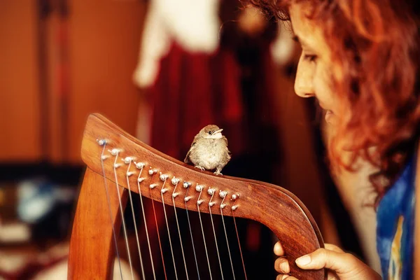 Jonge vrouw spelen Keltische harp en kleine vogel. — Stockfoto