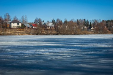 Arka planda bir köy ile erken ilkbahar göl donmuş