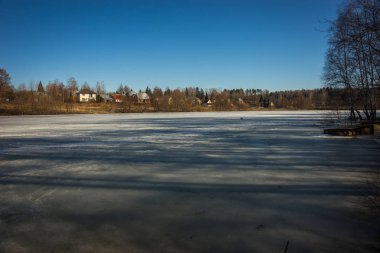 Arka planda bir köy ile erken ilkbahar göl donmuş