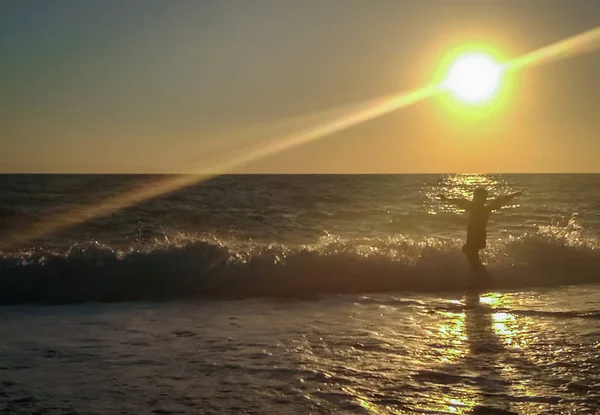 Силуэт мальчика на фоне волны с брызгами на солнце — стоковое фото