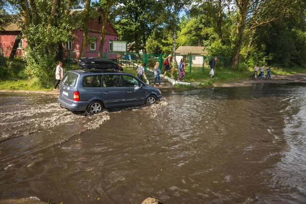 Car moving deep in  puddle after  rain on Baltic spit — Stock Photo, Image