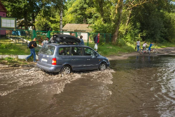 Car moving deep in  puddle after  rain on Baltic spit — Stock Photo, Image