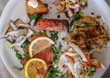 Beyaz tabakta servis edilen çeşitli balık ve deniz ürünleri.