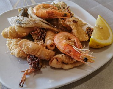 Karışık deniz ürünleri ve limonlu balıklar beyaz tabakta.