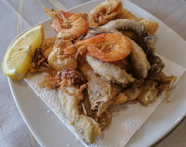 Karışık deniz ürünleri ve limonlu balıklar beyaz tabakta.