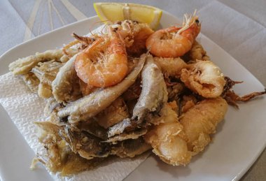 Karışık deniz ürünleri ve limonlu balıklar beyaz tabakta.