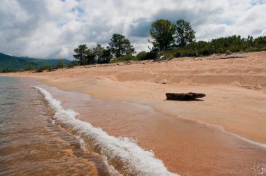 Rusya 'nın Irkutsk bölgesindeki Baykal Gölü' nün kumlu sahili, dalgalar ve kütükler görünüyor.