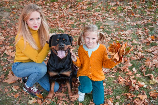 Hermosa familia feliz se divierte con el perro Rottweiler. Rubia adorable madre e hija abrazando a su perro . — Foto de Stock