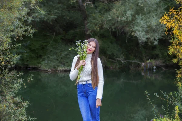 Utomhus porträtt av vacker ung brunett kvinna med långt hår och blommor i parken — Stockfoto