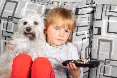 Kanepede televizyon izleyen genç sarışın kız beyaz Schnauzer köpek yavrusuyla. Tecritteki çocuklar, karantina.