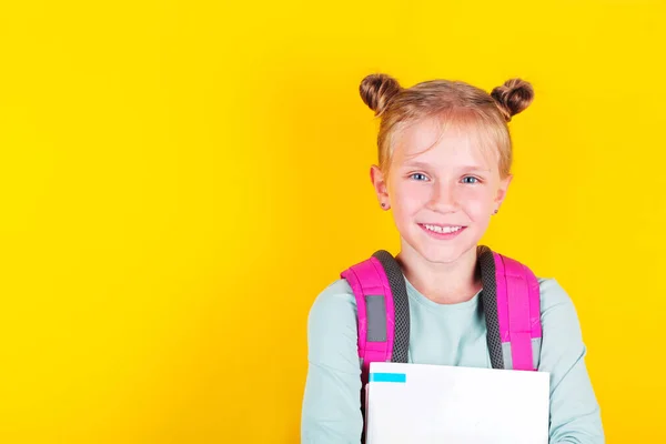 Girl from elementary school with book and backpack on yellow background. School concept, education. Back to School. — Stock Photo, Image