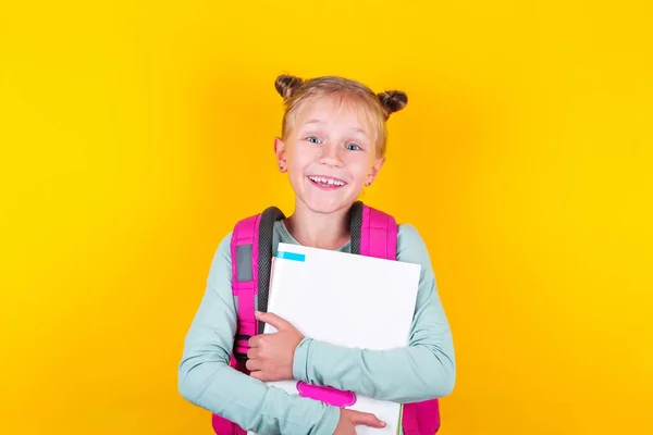 Girl from elementary school with book and backpack on yellow background. School concept, education. Back to School. — Stock Photo, Image