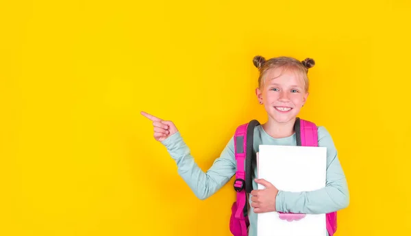 Girl from elementary school with book and backpack on yellow background. School concept, education. Back to School. — Stock Photo, Image