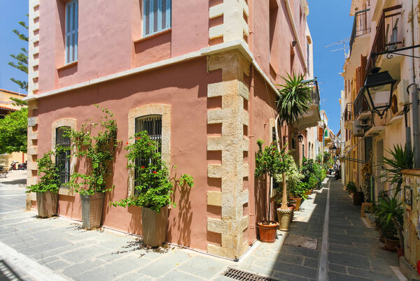 Rethymnon, Island Crete, Greece, - June 23, 2016: The narrow street of the old town's part of city Rethymnon and red colored house with plants and flowers in the big pots in hot sunny summer day