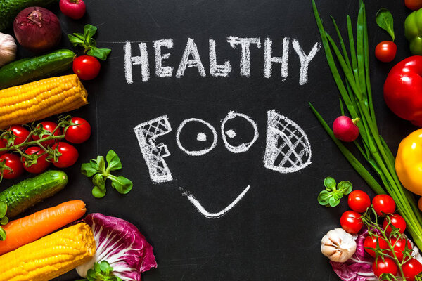 Photo of a table top full of fresh vegetables or healthy food background. Healthy food concept with fresh vegetables for cooking.Title "Healthy food" with smile is written by chalk on the middle of dark background.