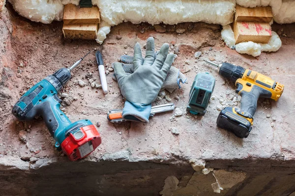 Some tools - drill, screwdriver, mounting knife, mounting electronic level and worker\'s gloves are on the windowsill during under renovation, remodeling and construction of apartment.