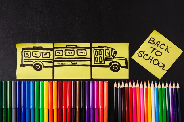 Повернутися до шкільного фону з великою кількістю барвистих ручок з фетру і барвистими олівцями, заголовками "Назад до школи" і малюнком шкільного автобуса, намальованого на жовтих шматочках паперу на чорній шкільній дошці — стокове фото