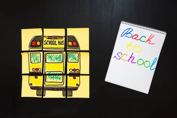 Back to school background with title "Back to school" and "school bus" written on the yellow pieces of paper and notebook with title "Back to school" are on the chalkboard — Stock Photo, Image