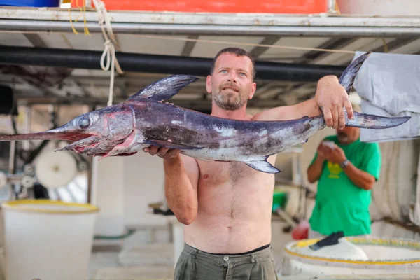 Bali, Island Crete, Greece, - June 30, 2016: Man is a fisherman carries a big fish (sawfish) after successful fish catch from the fishing boat.