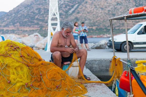 Bali, Island Girit, Yunanistan, - 30 Haziran 2016: yaşlı balıkçı net yakınındaki balıkçı teknesi Yunanistan Crete adada bulunan iskelede balık onarma.