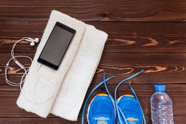 Fitness kavramı. Spor donatımı. Spor ayakkabı (spor ayakkabı), havlu, şişe suyu, kulaklık (kulaklık), telefonu üzerinde ahşap arka plan.