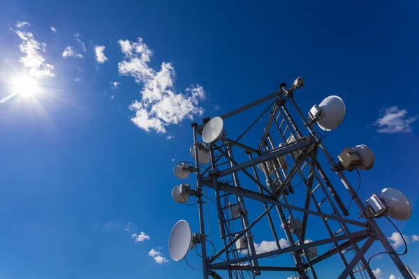 Torre de telecomunicaciones con microondas, antenas de radio y antenas parabólicas con sombras en el techo contra el cielo azul y el sol — Foto de Stock