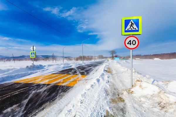 Опасная снежная дорога с пешеходным переходом, автобусной остановкой и дорожными знаками для вождения автомобилей и общественного транспорта во время метели или снежной бури . — стоковое фото
