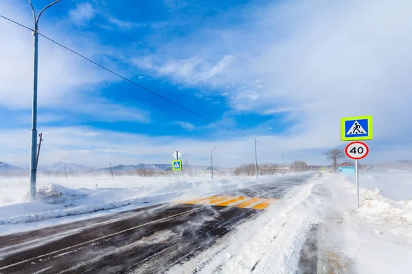 Опасная снежная дорога с пешеходным переходом, автобусной остановкой и дорожными знаками для вождения автомобилей и общественного транспорта во время метели или снежной бури . — стоковое фото