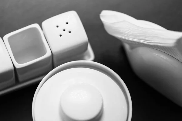 Zwart-wit beeld van zout en peper shakers, suikerpot en papier SERVETHOUDER in de houten tafel — Stockfoto