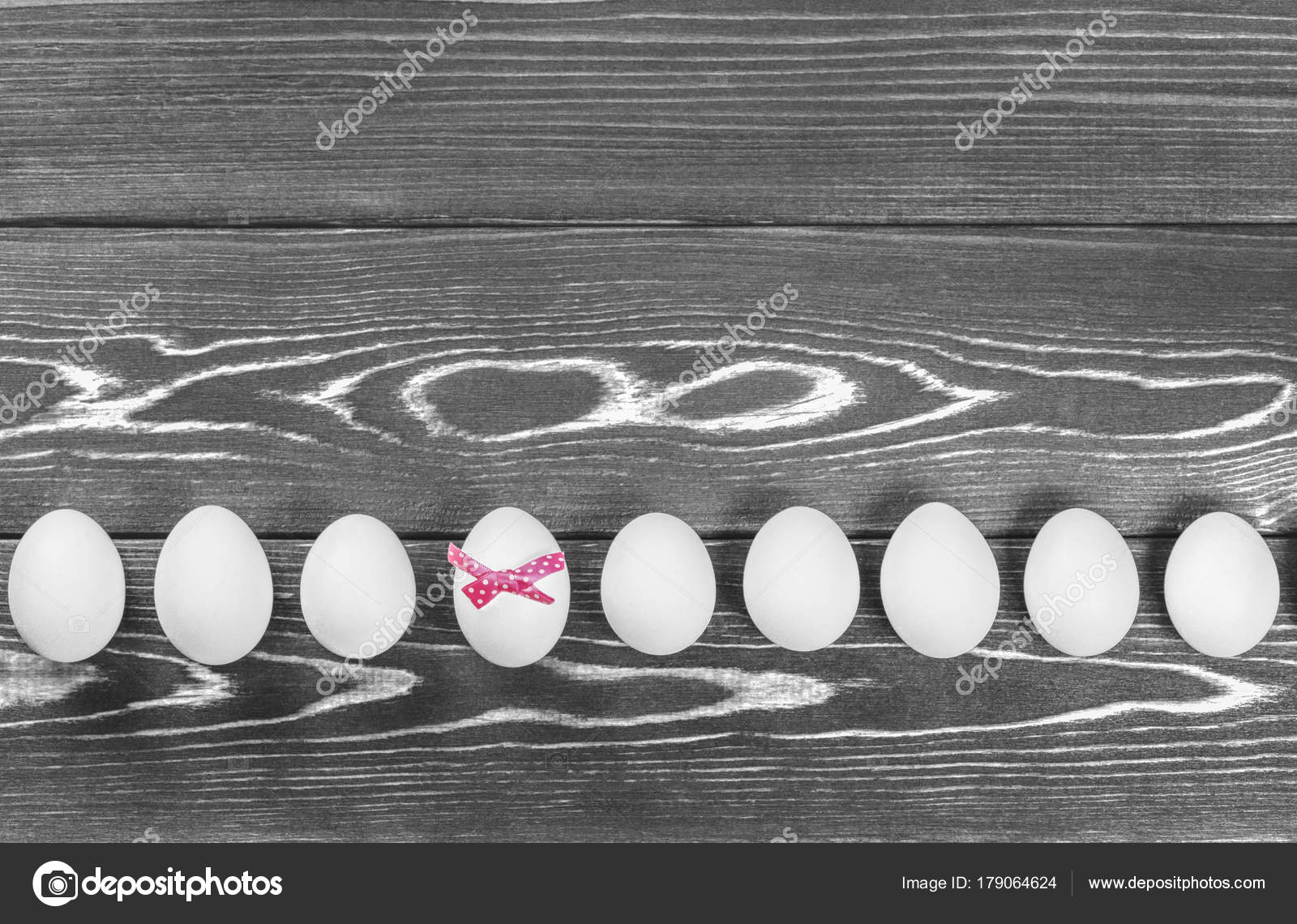 Black and white photo of the line of easter eggs are on the wooden background one of eggs has a pink bow stock image