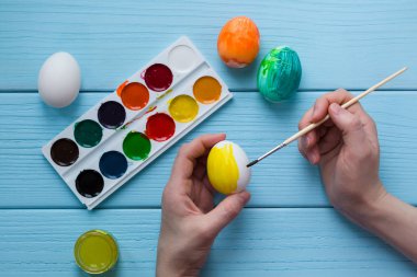Çocuklar el Paskalya yortusu yumurta sarı renk boya ve boya, boya fırçası, boyalı Paskalya yumurtaları mavi renkli ahşap arka plan üzerinde boya vardır.